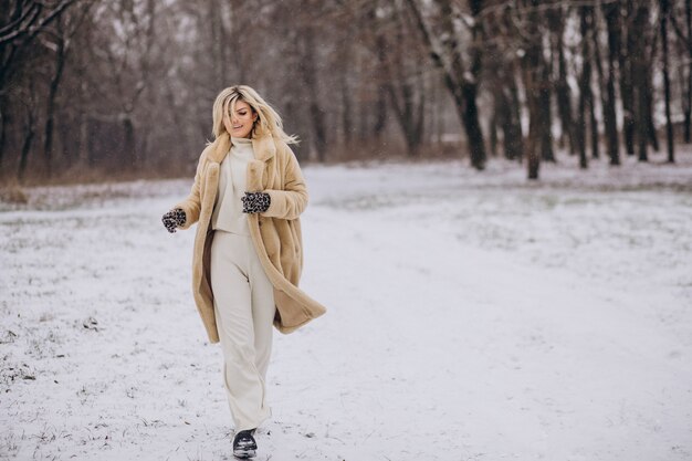 Hermosa mujer en abrigo de invierno caminando en el parque lleno de nieve