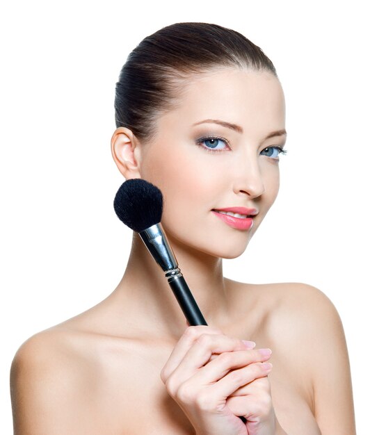 Hermosa mujer adulta joven sostiene el pincel de maquillaje para aplicar colorete o polvo aislado en blanco