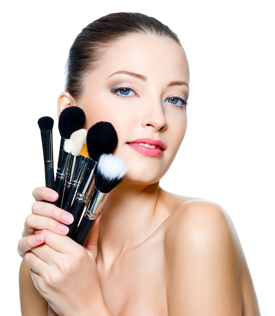 Foto gratuita hermosa mujer adulta joven sostiene los pinceles de maquillaje cerca de la cara atractiva. modelo de moda posando sobre fondo blanco.