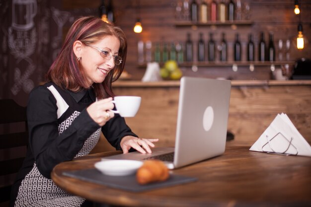 Hermosa mujer adulta sonriente disfrutando de un café mientras trabajaba en su cuaderno. Beber café en cafetería vintage