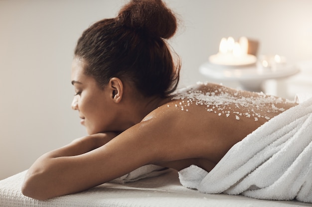 Hermosa mujer africana descansando relajante con sal de mar en la espalda en el salón de spa.