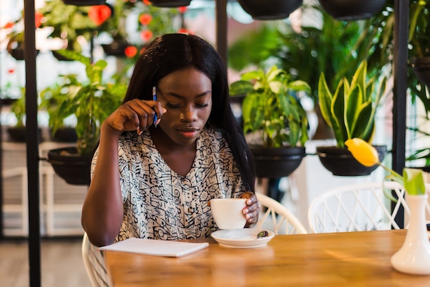 Hermosa mujer africana está tomando notas en la cafetería