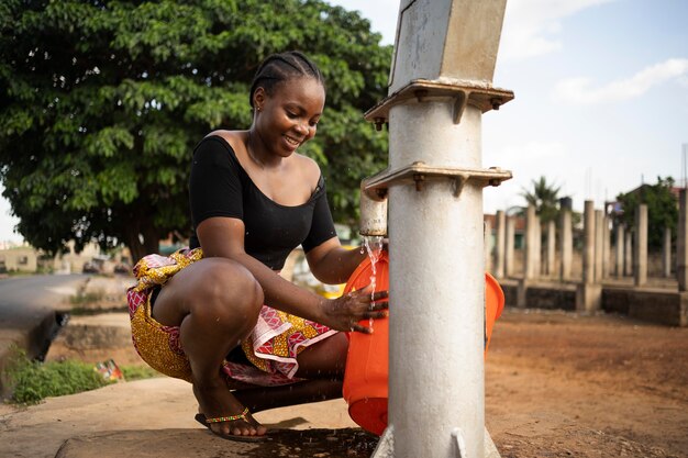 Hermosa mujer africana poniendo un poco de agua en un balde