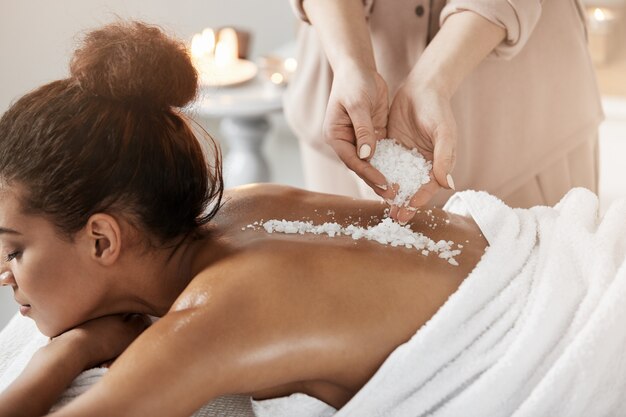 Hermosa mujer africana relajante disfrutando de masaje de salud spa con sal marina.