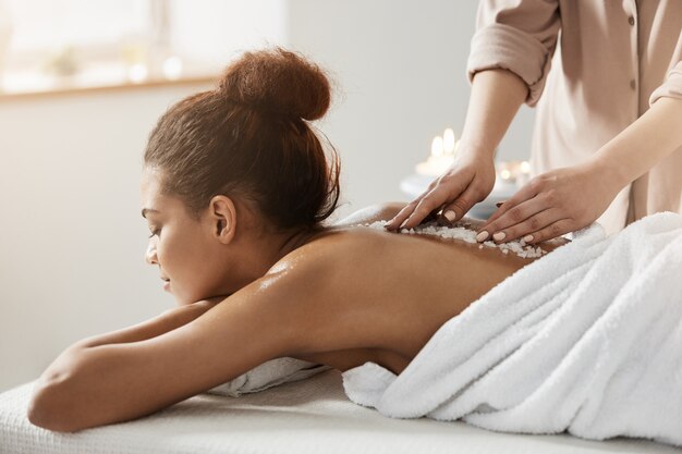 Hermosa mujer africana relajante disfrutando de masaje de salud spa con sal marina.