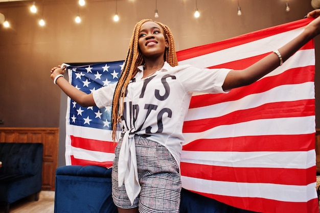 Hermosa mujer africana con ropa informal elegante posando con la bandera de Estados Unidos en la oficina