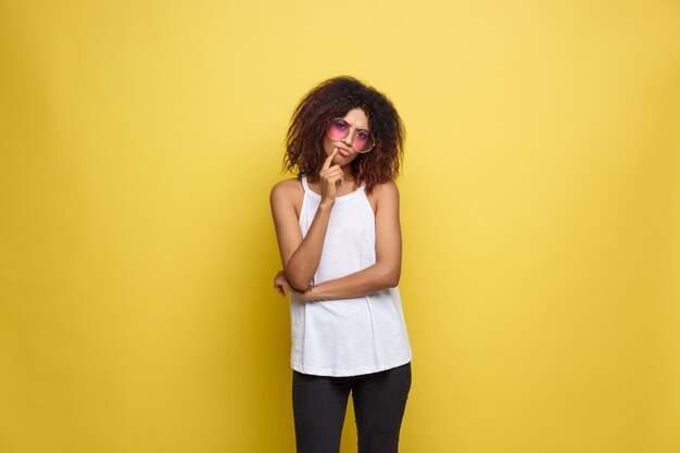 Hermosa mujer afroamericana atractiva con gafas de moda publicar sobre fondo de estudio amarillo. Espacio De La Copia.