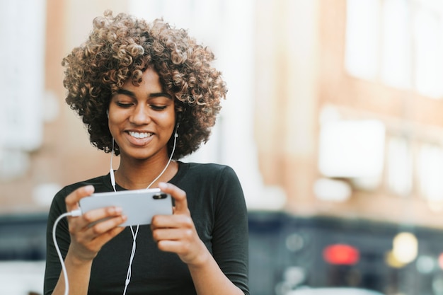 Hermosa mujer afroamericana con auriculares en los medios de comunicación remezclados de la ciudad