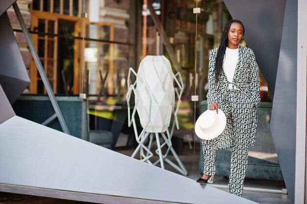 Hermosa mujer afroamericana con maquillaje natural, ropa de moda, código de vestimenta informal en blanco y negro, estilo de oficina, blusa total y pantalones, traje y sombrero.