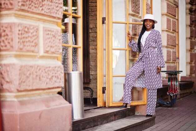 Hermosa mujer afroamericana con maquillaje natural, ropa de moda, código de vestimenta informal en blanco y negro, estilo de oficina, blusa total y pantalones, traje y sombrero.