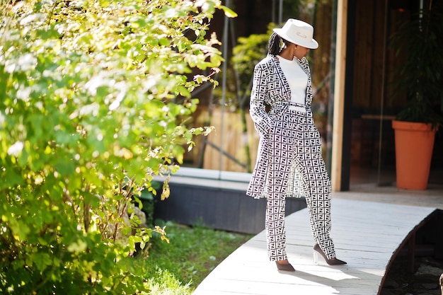 Hermosa mujer afroamericana con maquillaje natural, ropa de moda, código de vestimenta informal en blanco y negro, estilo de oficina, blusa total y pantalones, traje y sombrero.