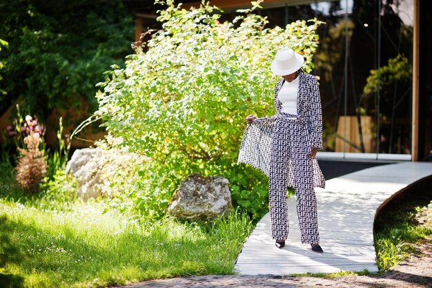 Hermosa mujer afroamericana con maquillaje natural, ropa de moda, código de vestimenta informal en blanco y negro, estilo de oficina, blusa total y pantalones, traje y sombrero.