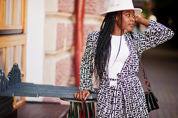 Hermosa mujer afroamericana con maquillaje natural, ropa de moda, código de vestimenta informal en blanco y negro, estilo de oficina, blusa total y pantalones, traje y sombrero.