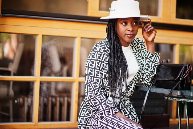 Hermosa mujer afroamericana con maquillaje natural, ropa de moda, código de vestimenta informal en blanco y negro, estilo de oficina, blusa total y pantalones, traje y sombrero.