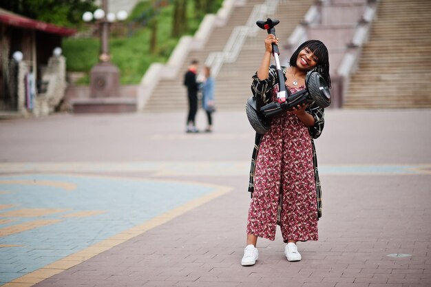 Hermosa mujer afroamericana sostenga las manos segway o hoverboard Chica negra con scooter eléctrico autoequilibrado de doble rueda