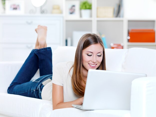 Hermosa mujer alegre acostada en el sofá con laptop