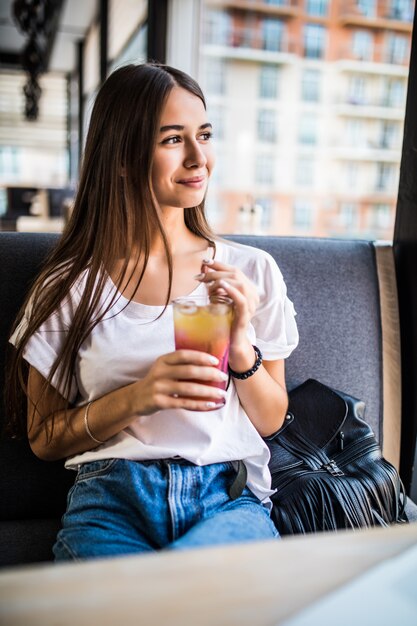 Hermosa mujer alegre freelancer de buen humor, usando una computadora portátil, sentado en cafés, bebiendo Mojitos.