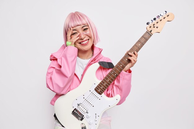 Hermosa mujer alegre músico toca la guitarra eléctrica siendo miembro del popular grupo de rock tiene un peinado rosa y lleva una chaqueta