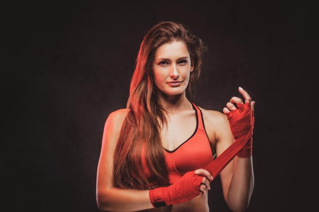 Hermosa mujer alegre en sujetador rojo está usando sus guantes antes de boxear.