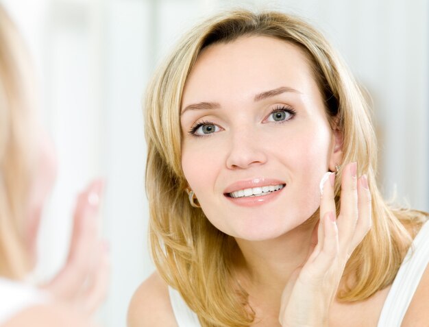 Hermosa mujer aplicando crema cosmética en la cara