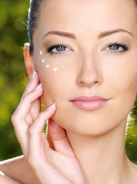 Hermosa mujer aplicando crema cosmética en la piel cerca de los ojos