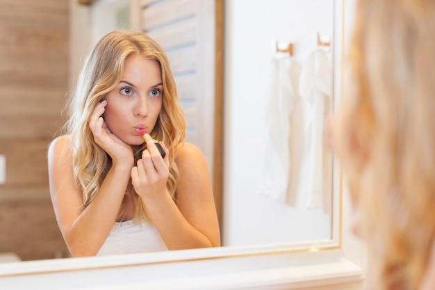 Hermosa mujer aplicando lápiz labial en el baño.