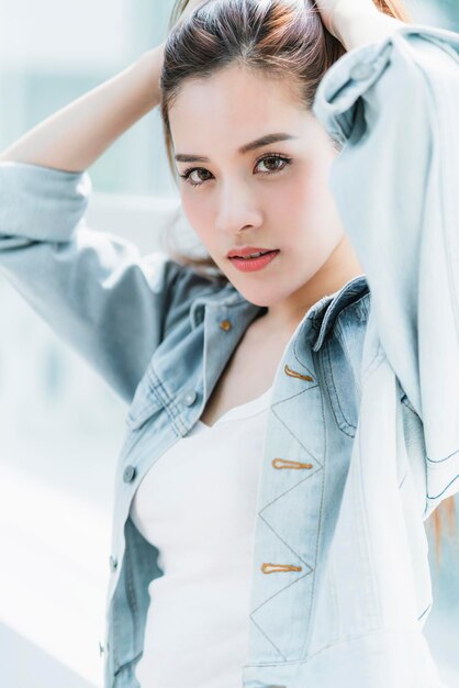 Hermosa mujer asiática con cabello castaño largo retrato camiseta blanca y traje de chaqueta de jean concepto de estilo de elevación