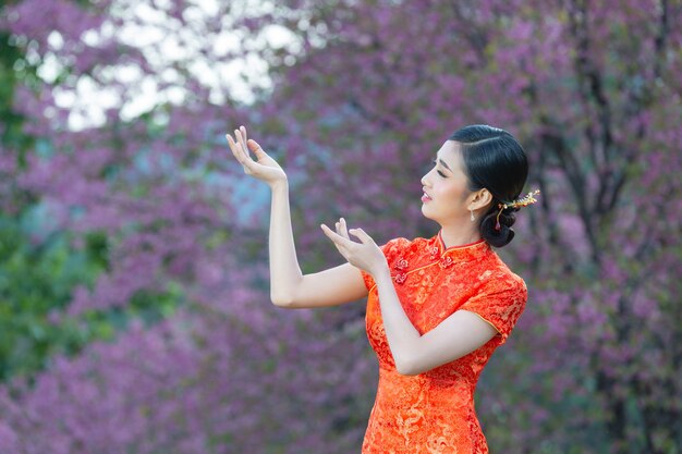 Hermosa mujer asiática feliz sonríe y te muestra algo en el año nuevo chino sobre fondo rosa.