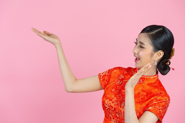 Hermosa mujer asiática feliz sonríe y te muestra algo en el año nuevo chino sobre fondo rosa.