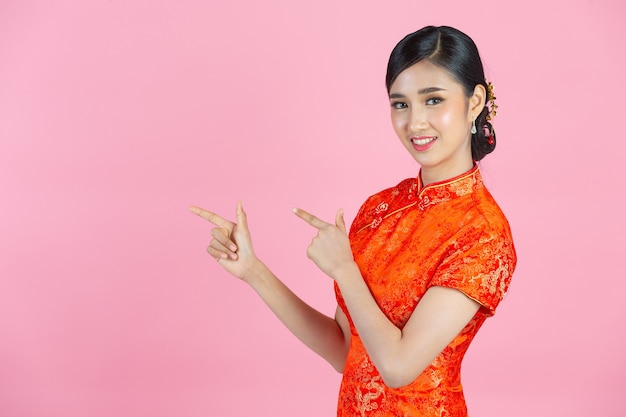 Hermosa mujer asiática feliz sonríe y te muestra algo en el año nuevo chino sobre fondo rosa.