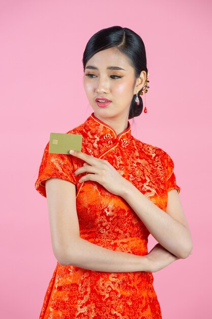 Hermosa mujer asiática feliz sonrisa y mostrar tarjeta de crédito en año nuevo chino sobre fondo rosa.