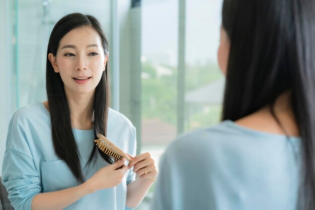 Hermosa mujer asiática maquillada y peinada con espejo en el baño con luz matutina