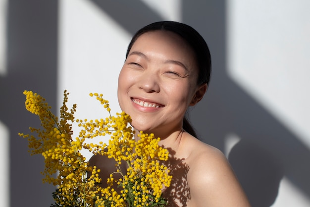 Hermosa mujer asiática posando sosteniendo flores amarillas con una piel perfecta