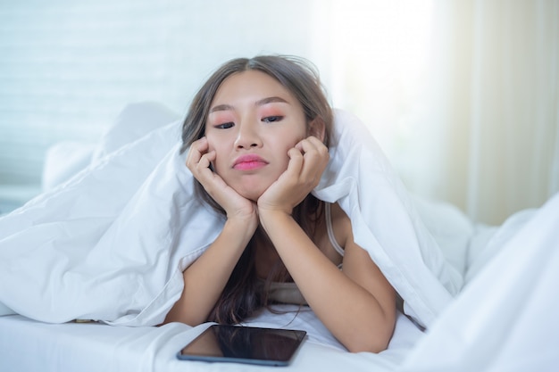 Una hermosa mujer asiática se relaja y trabaja con una computadora portátil, leyendo en casa.