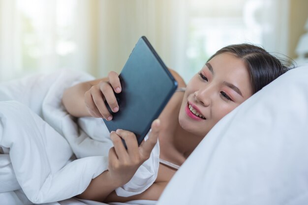 Una hermosa mujer asiática se relaja y trabaja con una computadora portátil, leyendo en casa.