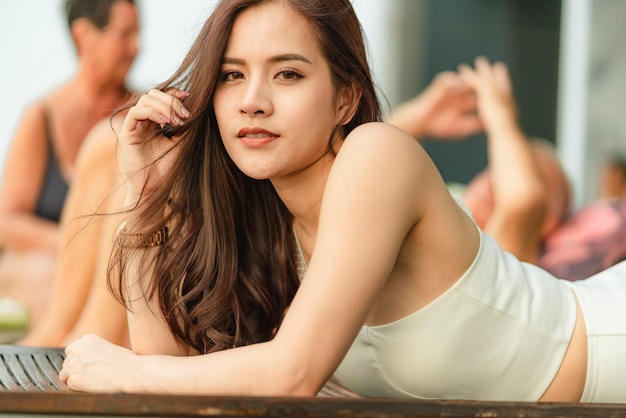 Hermosa mujer asiática relajarse tomando el sol vestido blanco cerca de la piscina temporada de verano