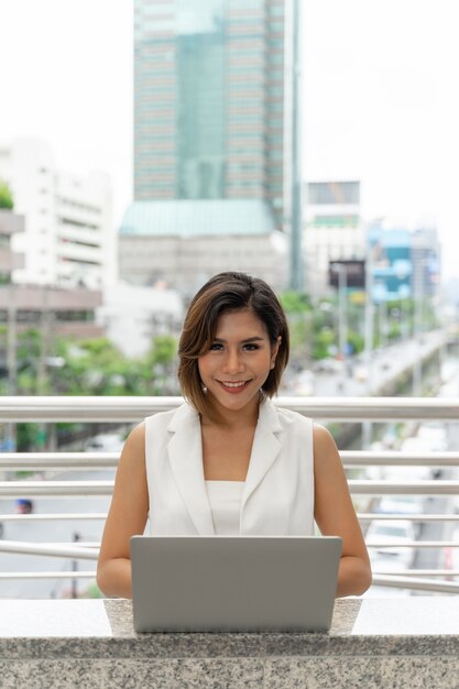 Hermosa mujer asiática sonriendo en ropa de mujer de negocios con computadora portátil y teléfono inteligente