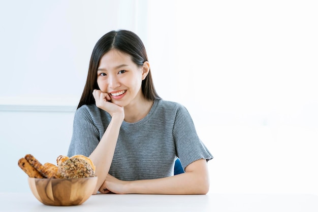 Hermosa mujer asiática vestido casual sentarse y sonreír con un tazón de pan concepto de ideas de alimentos dietéticos