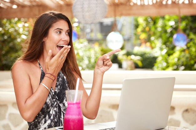 Hermosa mujer asombrada mira con entusiasmo en la distancia, trabaja en la computadora portátil