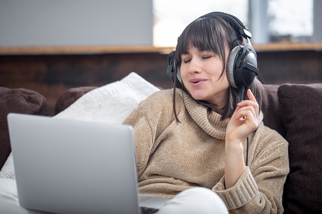 Hermosa mujer en auriculares escuchando música en casa en el sofá con una computadora portátil.