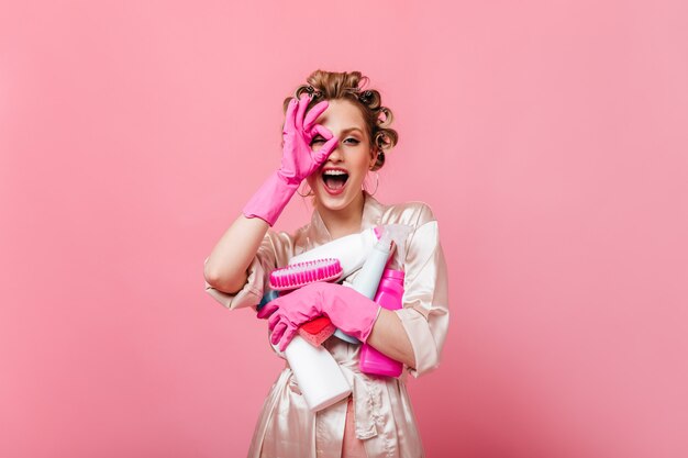 Hermosa mujer en bata rosa muestra signo bien y tiene detergente