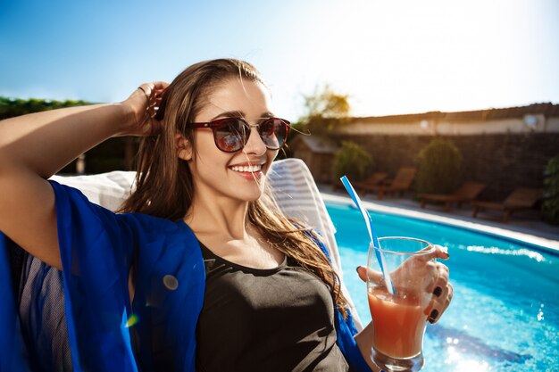 Hermosa mujer bebiendo cócteles, tumbado en una tumbona junto a la piscina