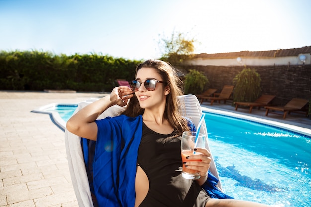 Hermosa mujer bebiendo cócteles, tumbado en una tumbona junto a la piscina