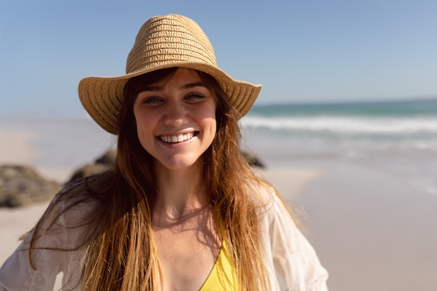 Hermosa mujer en bikini y sombrero mirando a la cámara en la playa bajo el sol