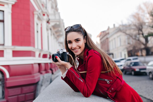 Hermosa mujer blanca en elegante traje rojo tomando foto de vista a la calle