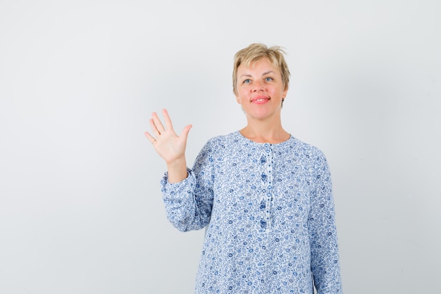 Hermosa mujer en blusa estampada agitando la mano para despedirse, vista frontal.