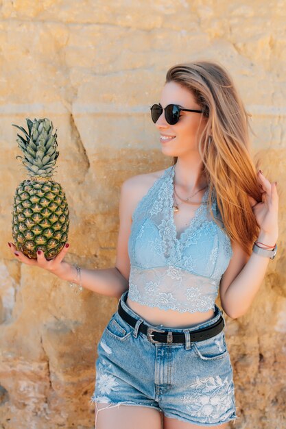 Hermosa mujer bonita con pelo rizado está sosteniendo piñas en la playa