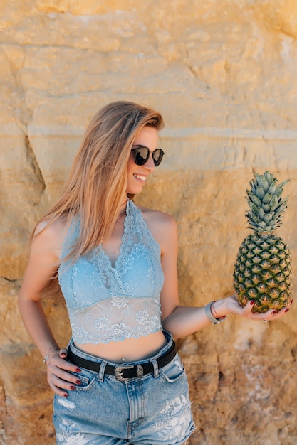 Hermosa mujer bonita con pelo rizado está sosteniendo piñas en la playa