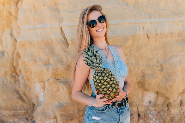 Hermosa mujer bonita con pelo rizado está sosteniendo piñas en la playa