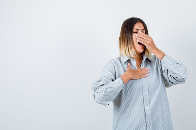 Hermosa mujer bostezando en camisa y mirando soñolienta, vista frontal.